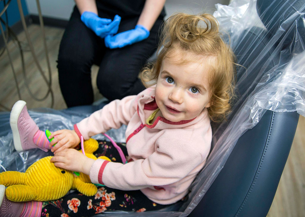 young blonde girl sitting in the dentist chair with a stuffed animal on her lap