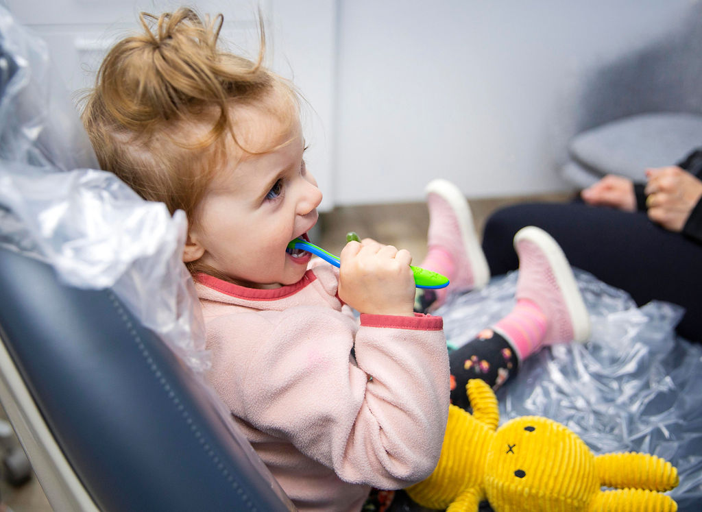 Young girl sitting in a dental chair brushing her teeth