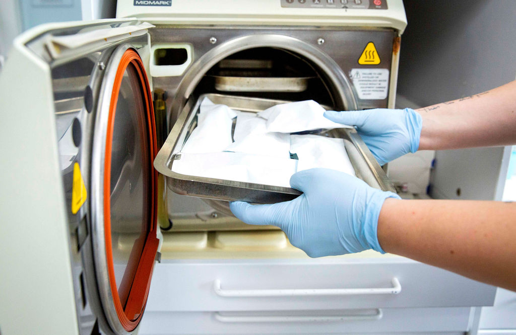 Gloved hands retrieving bagged dental tools on a tray